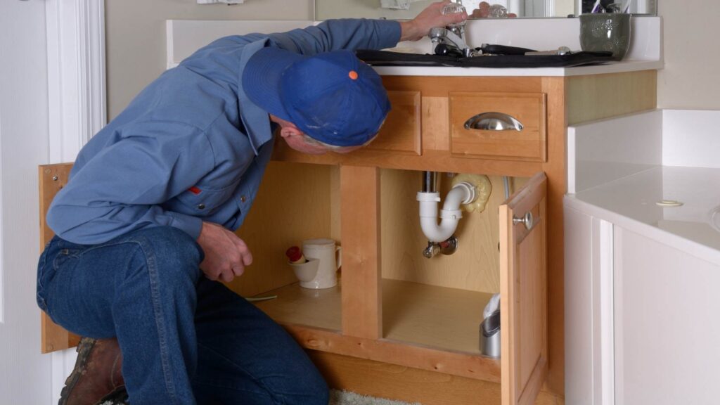 What is a Home Warranty, Blog Post, Image of a plumber fixing a leak in a bathroom sink